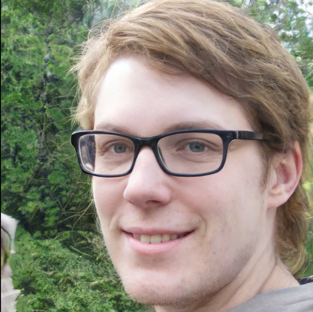 A guy with light stubble and glasses looks at the camera